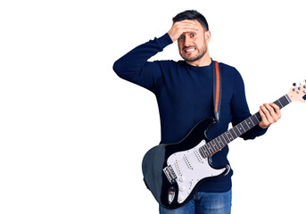 Young handsome man playing electric guitar stressed and frustrated with hand on head, surprised and angry face