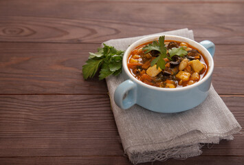 Bean soup with olives in a blue ceramic cup on a gray linen napkin on a wooden background. Vegetarian food. Copy spaes.