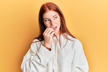 Young red head girl wearing casual sweatshirt looking stressed and nervous with hands on mouth biting nails. anxiety problem.