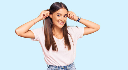 Young hispanic woman wearing casual white tshirt smiling pulling ears with fingers, funny gesture....