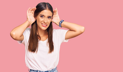 Fototapeta na wymiar Young hispanic woman wearing casual white tshirt trying to hear both hands on ear gesture, curious for gossip. hearing problem, deaf