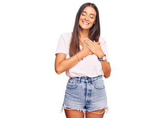 Obraz premium Young hispanic woman wearing casual white tshirt smiling with hands on chest with closed eyes and grateful gesture on face. health concept.