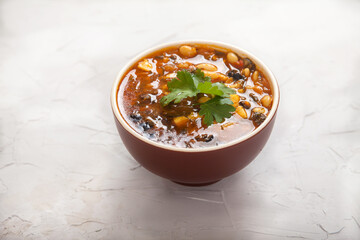 Bean soup in an earthenware dish with tomatoes, olives and parsley on a white concrete background.