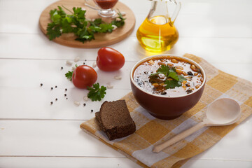 Bean and olive soup, rye bread, tomatoes, a wooden spoon and a bottle of olive oil on a white wooden background.