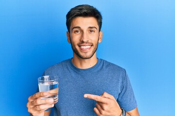 Young handsome man drinking glass of water smiling happy pointing with hand and finger