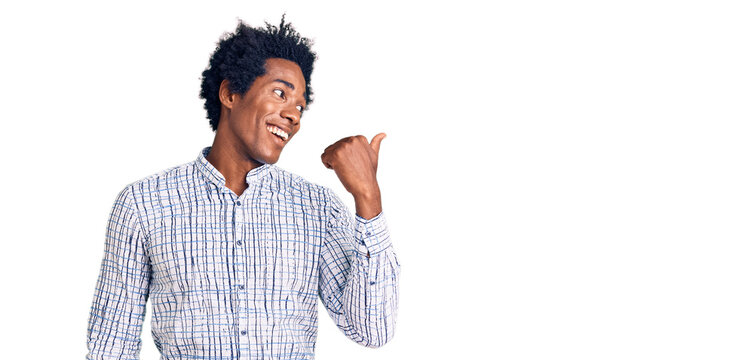Handsome african american man with afro hair wearing casual clothes smiling with happy face looking and pointing to the side with thumb up.