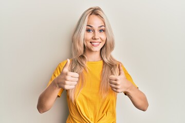 Obraz premium Beautiful caucasian blonde girl wearing casual tshirt success sign doing positive gesture with hand, thumbs up smiling and happy. cheerful expression and winner gesture.