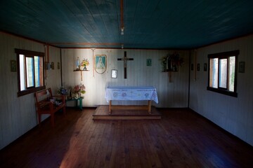 intérieur d'une petite chapelle vide en bois au Chili très simple et rudimentaire avec un rayon de lumière illuminant le mur du fond
