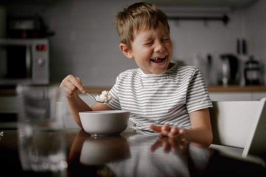 cute caucasian 6 year old boy eating oatmeals for breakfast and laughing. Image with selective focus