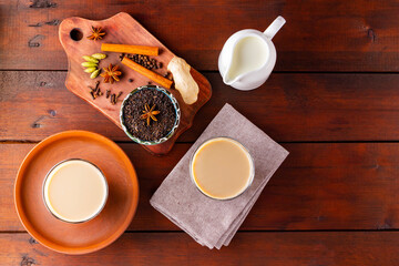 Two glasses of masala tea and various ingredients. Masala chai tea on wooden boards. Milk tea and spices. Copy space. Top view