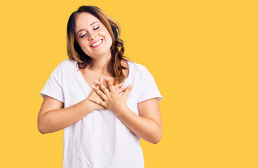 Young beautiful caucasian woman wearing casual white tshirt smiling with hands on chest with closed eyes and grateful gesture on face. health concept.