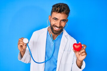 Young hispanic man wearing doctor uniform holding stethoscope and heart smiling and laughing hard...