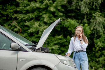 Young woman standing near broken down car with popped up hood having trouble with her vehicle. Waiting for help tow truck or technical support. A woman calls the service center