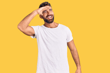 Fototapeta na wymiar Young hispanic man wearing casual white tshirt very happy and smiling looking far away with hand over head. searching concept.
