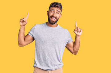 Young hispanic man wearing casual clothes smiling amazed and surprised and pointing up with fingers and raised arms.