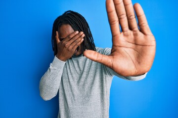 African american man with braids wearing turtleneck sweater covering eyes with hands and doing stop gesture with sad and fear expression. embarrassed and negative concept.