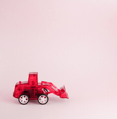 Colorful toy red plastic tractor isolated on pink background. Red excavator. Toy for children.
  Side view. Copyspace for text. Poster for advertising.