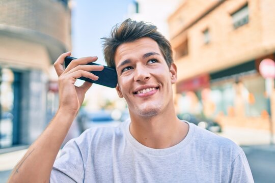 Young caucasian man smiling happy listening audio message using smartphone at the city.