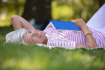 senior woman reading book laid on the grass