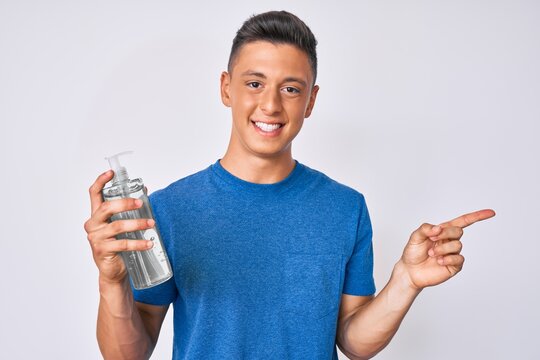 Young hispanic boy using hand sanitizer gel smiling happy pointing with hand and finger to the side