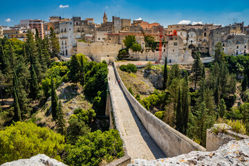 Fototapeta na wymiar Gravina in Puglia, Italy. The stone bridge, ancient aqueduct and viaduct. On the other side of the valley where the Gravina stream flows, the skyline of the city with its houses and palaces.