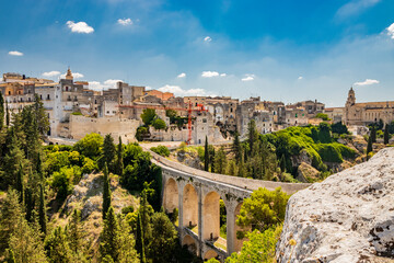 Fototapeta na wymiar Gravina in Puglia, Italy. The stone bridge, ancient aqueduct and viaduct. Across the valley the skyline of the city with its houses and buildings and the cathedral at the bottom.