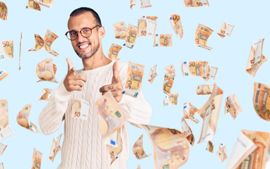 Young handsome man wearing casual clothes and glasses pointing fingers to camera with happy and funny face. good energy and vibes.
