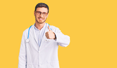 Handsome young man with bear wearing doctor uniform doing happy thumbs up gesture with hand. approving expression looking at the camera showing success.