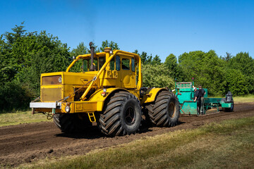 Closeup of a yellow tractor with heavy wheels in a field pulling a weight