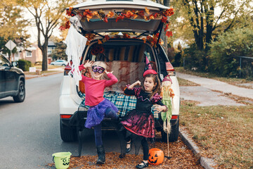 Trick or trunk. Children siblings sisters celebrating Halloween in trunk of car. Friends kids girls preparing for October holiday outdoors. Social distance and safe alternative celebration.