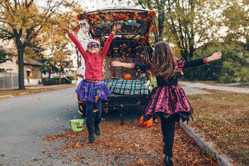 Trick or trunk. Children siblings sisters celebrating Halloween in trunk of car. Friends kids girls preparing for October holiday outdoors. Social distance and safe alternative celebration.