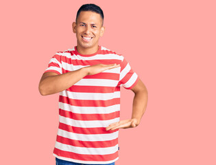 Young handsome latin man wearing casual clothes gesturing with hands showing big and large size sign, measure symbol. smiling looking at the camera. measuring concept.