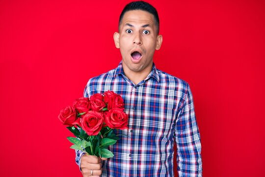 Young handsome latin man holding flowers scared and amazed with open mouth for surprise, disbelief face