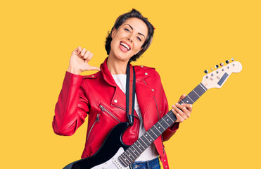 Young beautiful woman playing electric guitar pointing finger to one self smiling happy and proud