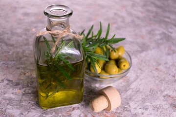 Olive oil with a branch of rosemary in a bottle on a gray background.
Close-up.