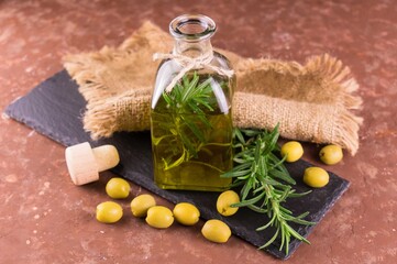 Olive oil with a branch of rosemary in a bottle on a brown background.
