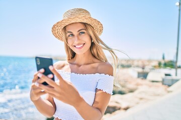 Fototapeta premium Young blonde tourist girl smiling happy using smartphone at the promenade.