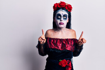 Young woman wearing mexican day of the dead makeup pointing up looking sad and upset, indicating direction with fingers, unhappy and depressed.