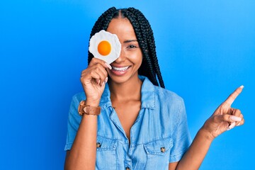 Beautiful hispanic woman holding fried egg smiling happy pointing with hand and finger to the side