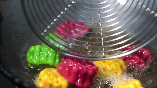 Slow motion 120fps shot of colorful Fryums being deep fried in hot oil bubbling and sizzling with bubbles forming and size increasing of this popular north indian snack and street food