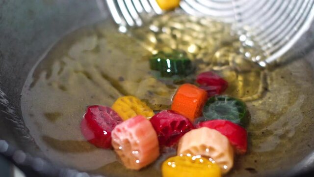 Slow motion 120fps shot of colorful Fryums being deep fried in hot oil bubbling and sizzling with bubbles forming and size increasing of this popular north indian snack and street food