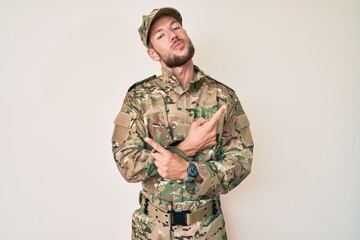 Young caucasian man wearing camouflage army uniform pointing to both sides with fingers, different direction disagree