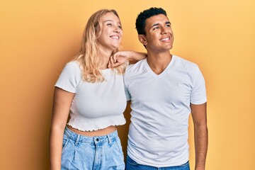 Young interracial couple wearing casual white tshirt looking away to side with smile on face, natural expression. laughing confident.
