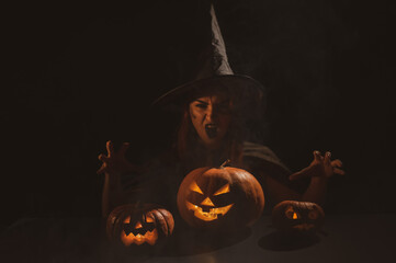 The evil witch casts a spell on pumpkins. Portrait of a woman in a carnival halloween costume in...