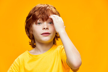 Red-haired boy touching face with hand and isolated yellow background