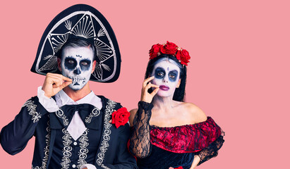 Young couple wearing mexican day of the dead costume over background mouth and lips shut as zip with fingers. secret and silent, taboo talking