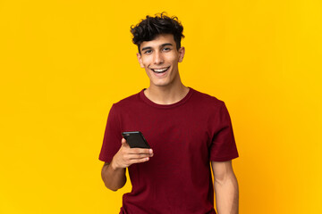 Young Argentinian man isolated on yellow background using mobile phone