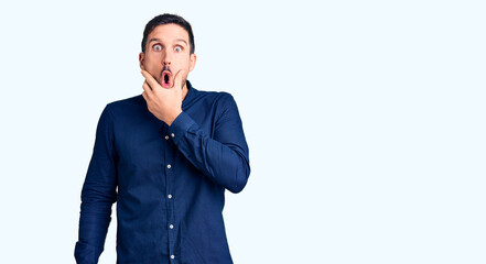 Young handsome man wearing casual shirt looking fascinated with disbelief, surprise and amazed expression with hands on chin