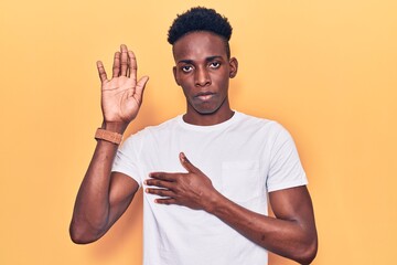 Young african american man wearing casual clothes swearing with hand on chest and open palm, making...