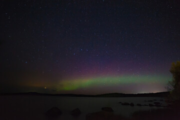 Fototapeta na wymiar View of the aurora borealis. Polar lights in the night starry sky over the lake.